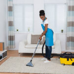 Young African Woman Cleaning Carpet with a Vaccum Cleaner